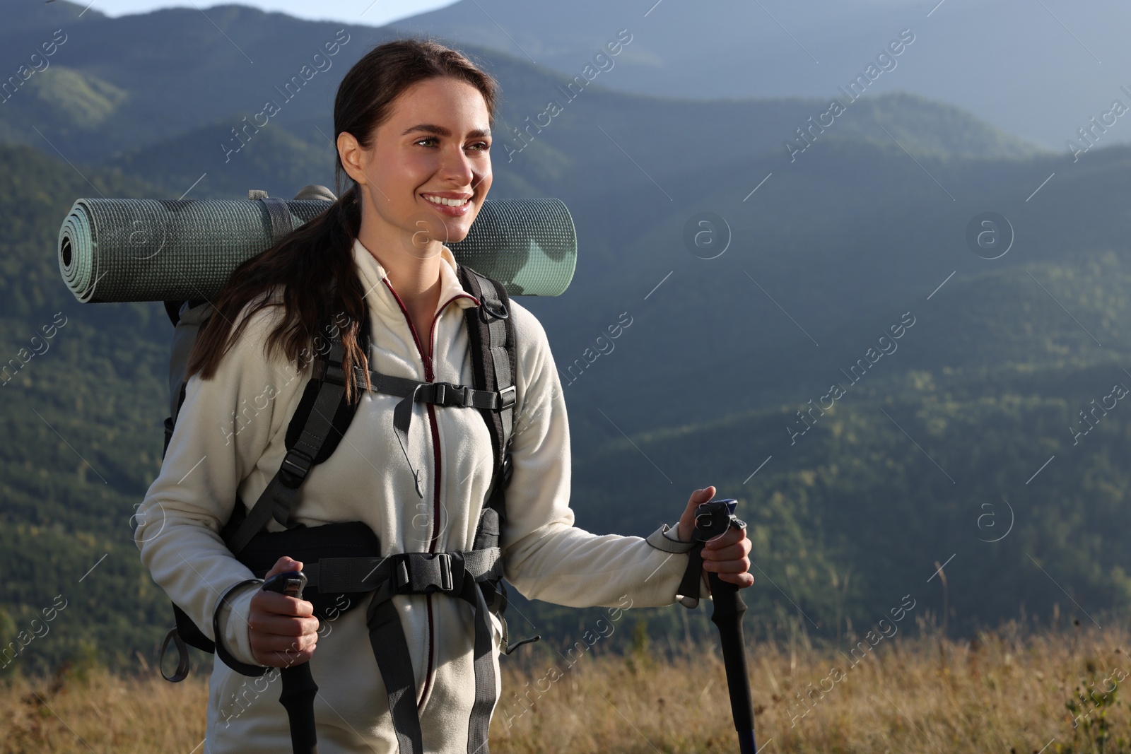 Photo of Tourist with backpack and trekking poles hiking through mountains, space for text