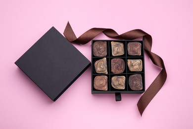 Box of tasty chocolate candies with ribbon on pink background, flat lay