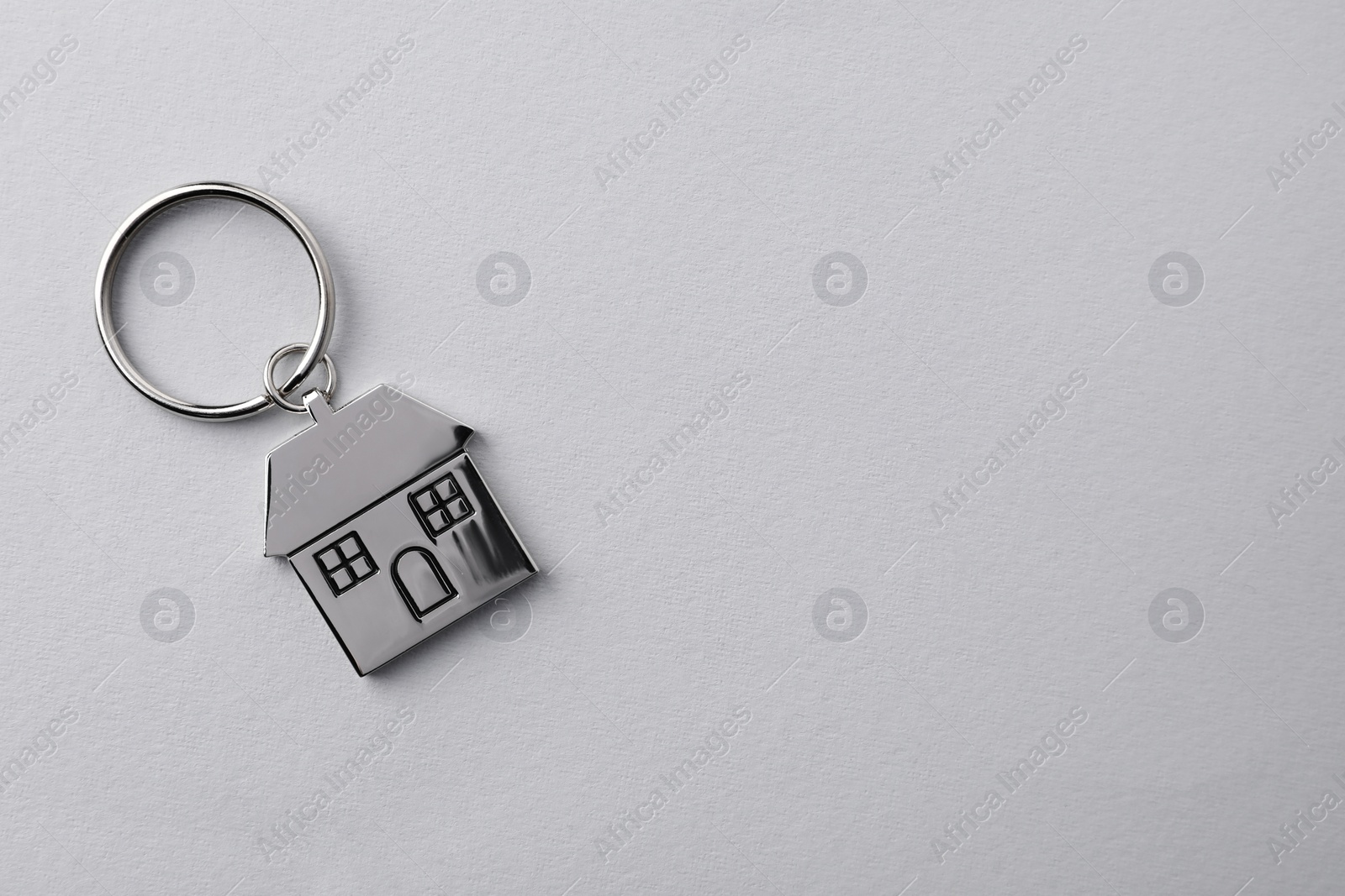 Photo of Metallic keychain in shape of house on light grey background, top view. Space for text