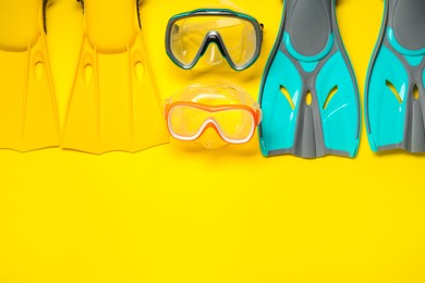 Photo of Different flippers and masks on yellow background, flat lay. Space for text