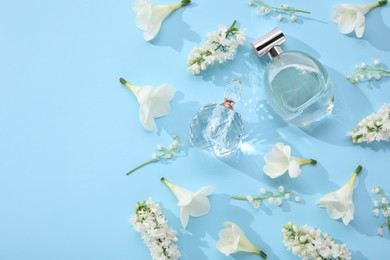 Photo of Luxury perfumes and floral decor on light blue background, flat lay. Space for text