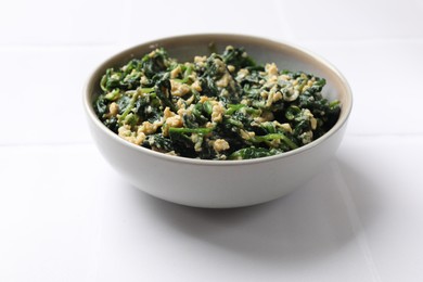 Photo of Tasty spinach dip with egg in bowl on white table, closeup