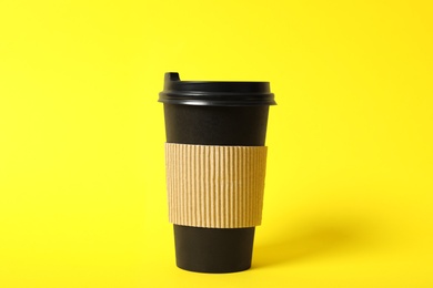 Photo of Takeaway paper coffee cup with cardboard sleeve on yellow background