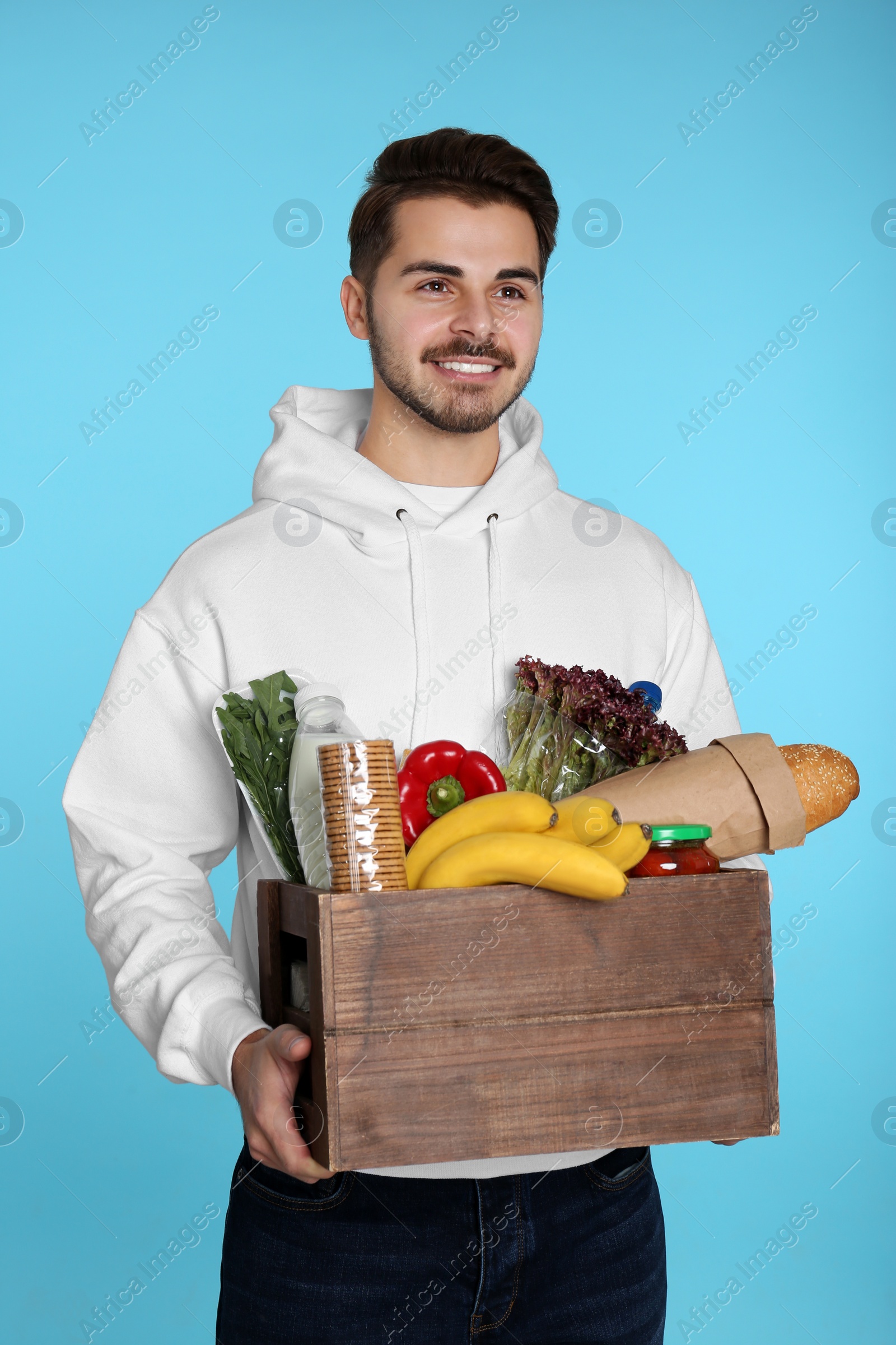 Photo of Young man holding wooden crate with products on color background. Food delivery service