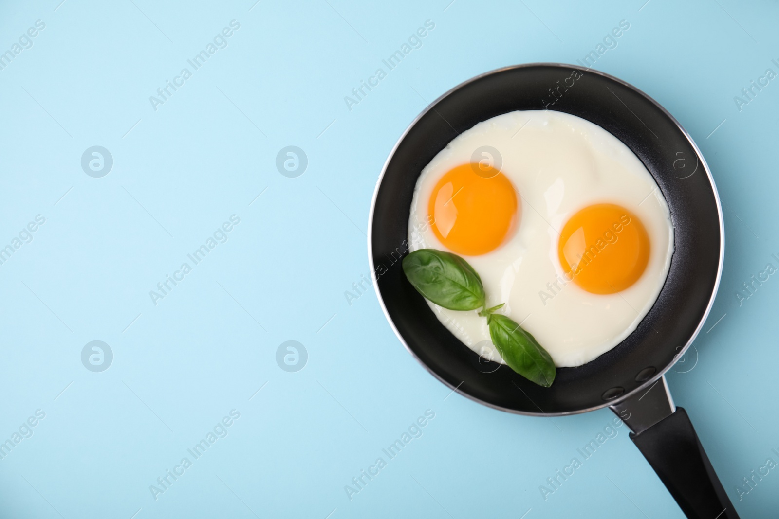 Photo of Tasty fried eggs with basil in pan on light blue background, top view