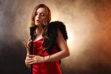 Photo of Beautiful young woman in stylish dress with microphone singing on dark background in color lights and smoke