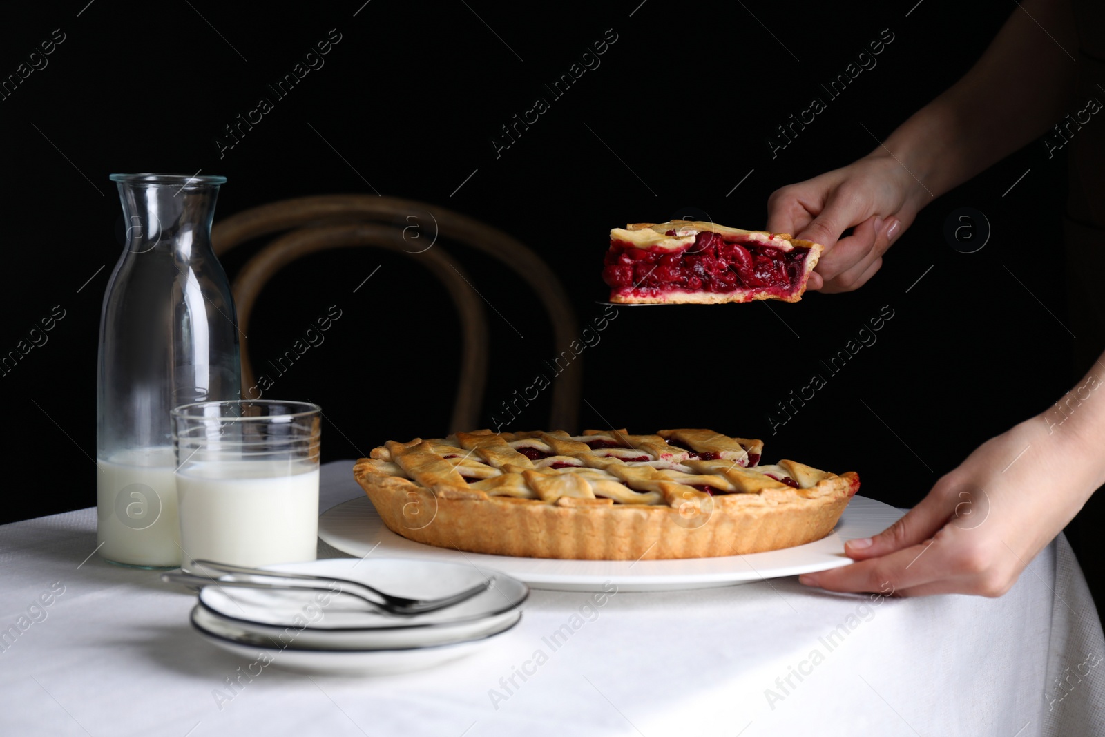 Photo of Woman taking slice of delicious cherry pie at table against dark background, closeup