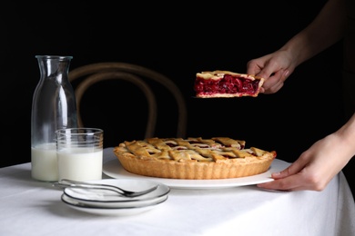 Photo of Woman taking slice of delicious cherry pie at table against dark background, closeup