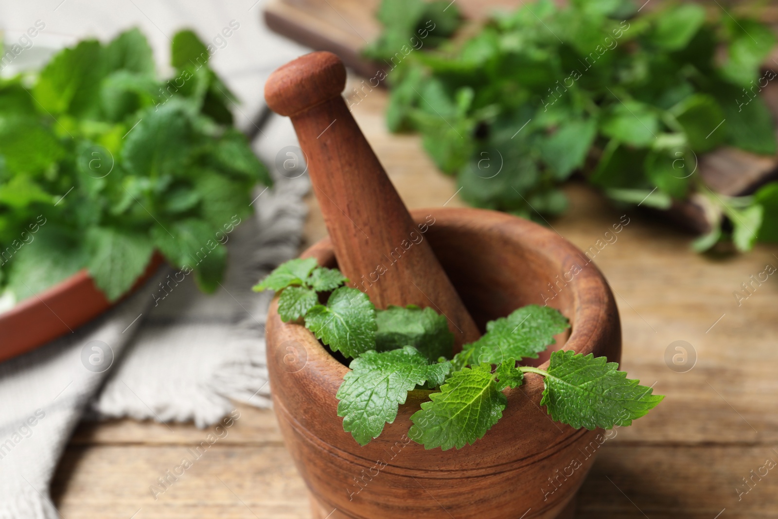 Photo of Mortar with pestle and fresh lemon balm on wooden table