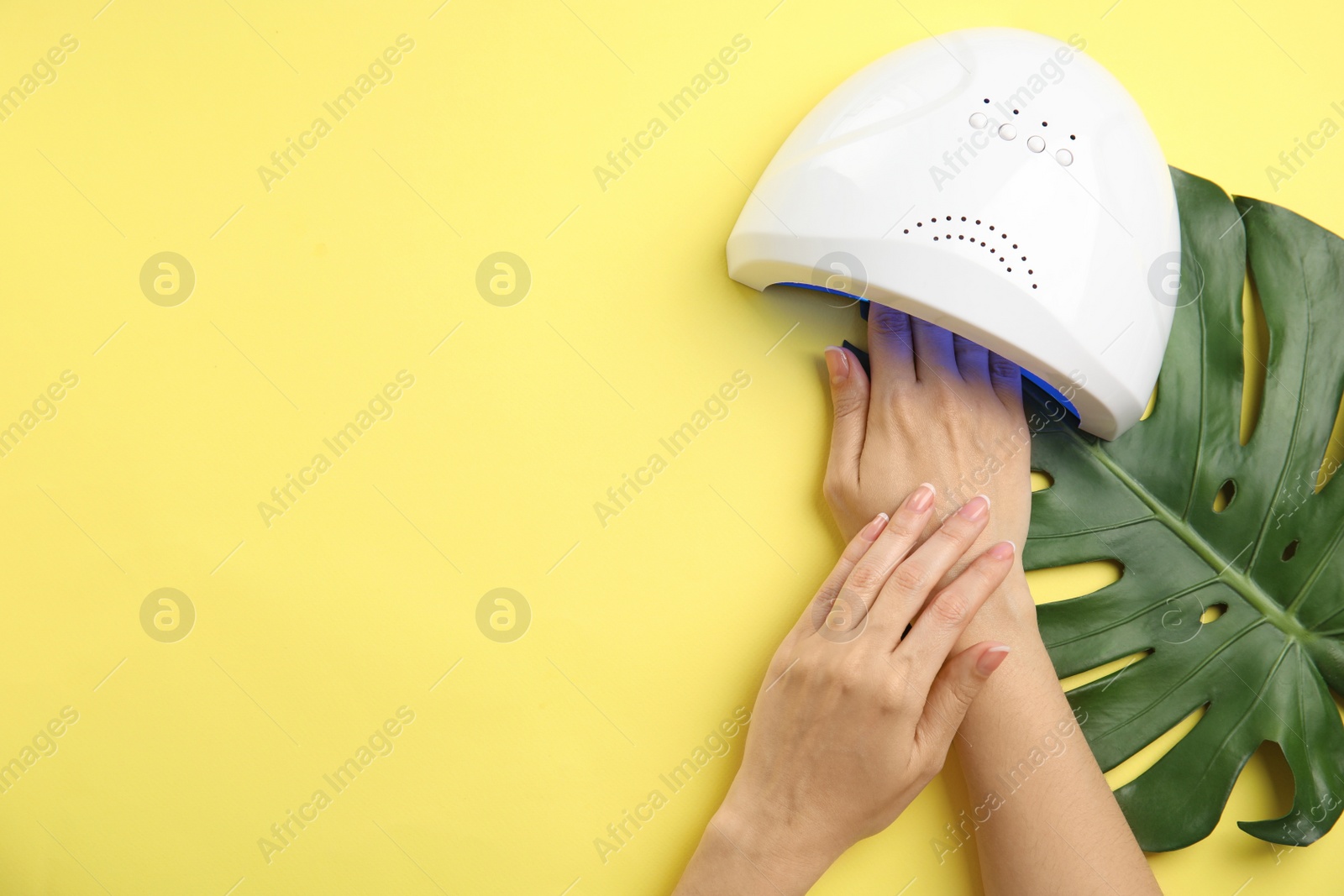 Photo of Woman using ultraviolet lamp to dry gel nail polish on yellow background, top view. Space for text