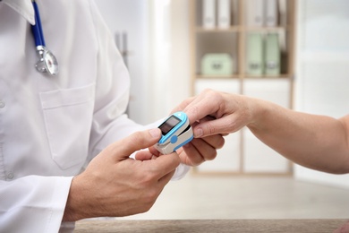 Photo of Doctor checking mature woman's pulse with medical device in hospital, closeup