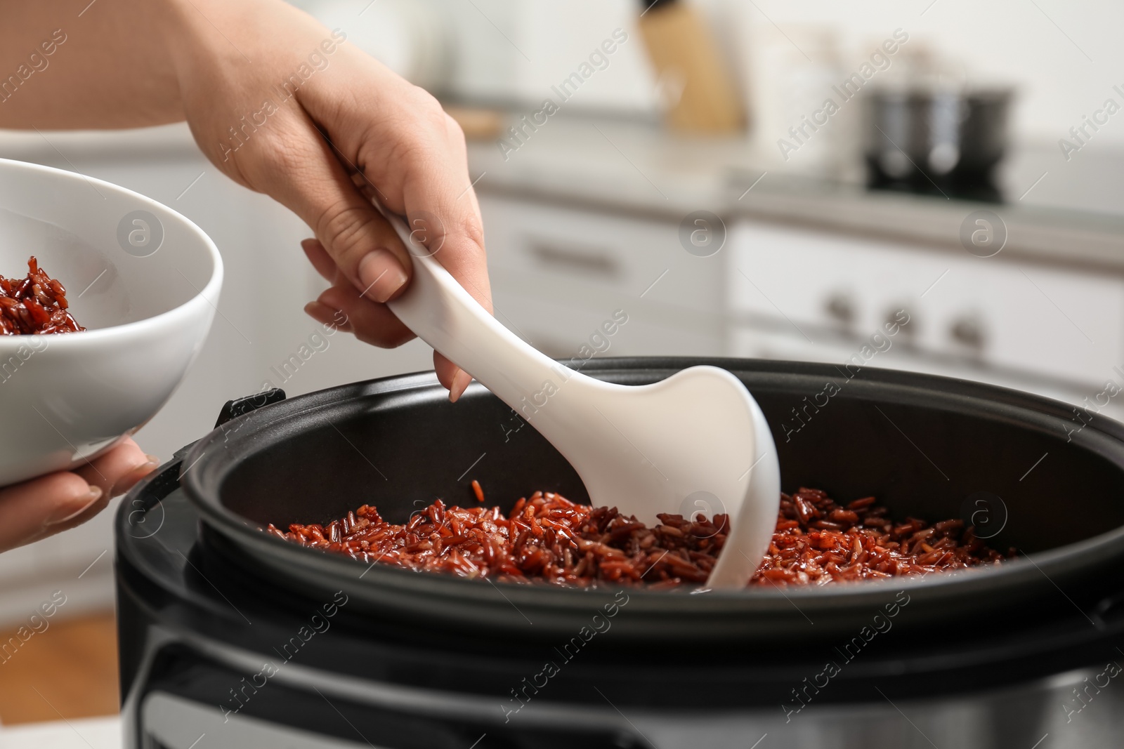 Photo of Woman putting brown rice into bowl from multi cooker in kitchen, closeup