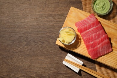 Photo of Tasty sashimi (pieces of fresh raw tuna) served with wasabi sauce and ginger slices on wooden table, top view. Space for text