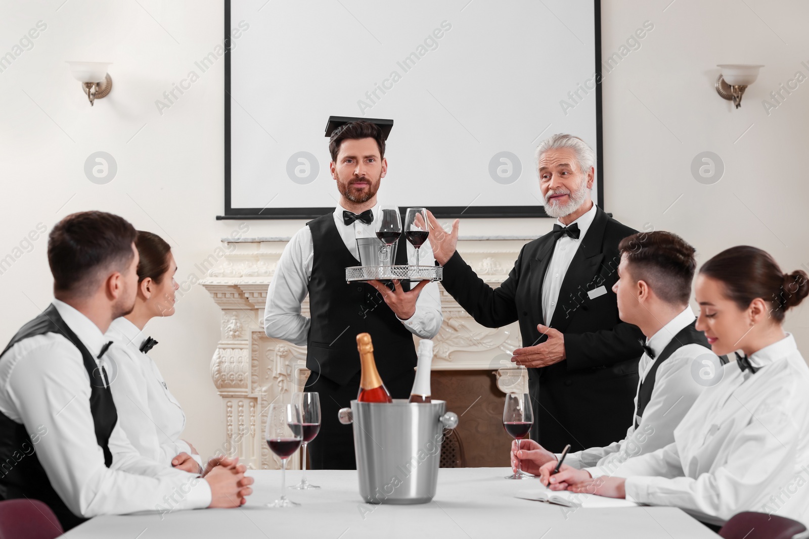 Photo of Senior man in formal suit teaching trainees indoors. Professional butler courses