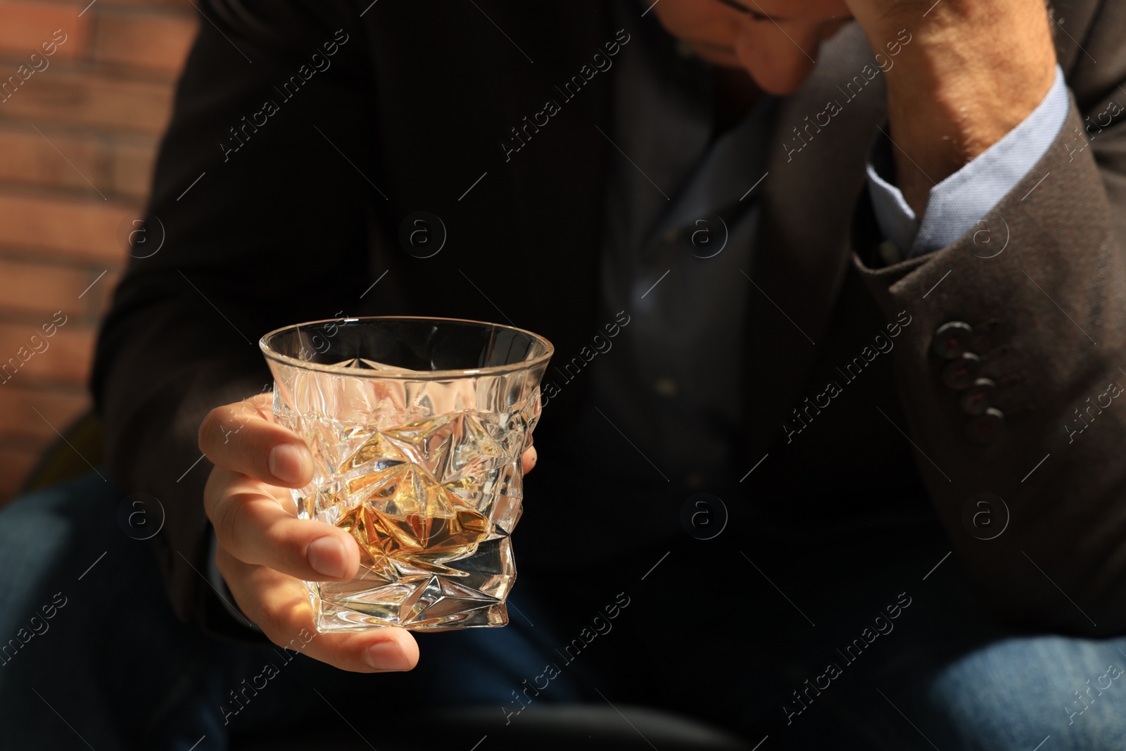 Photo of Addicted man with glass of alcoholic drink near red brick wall, closeup