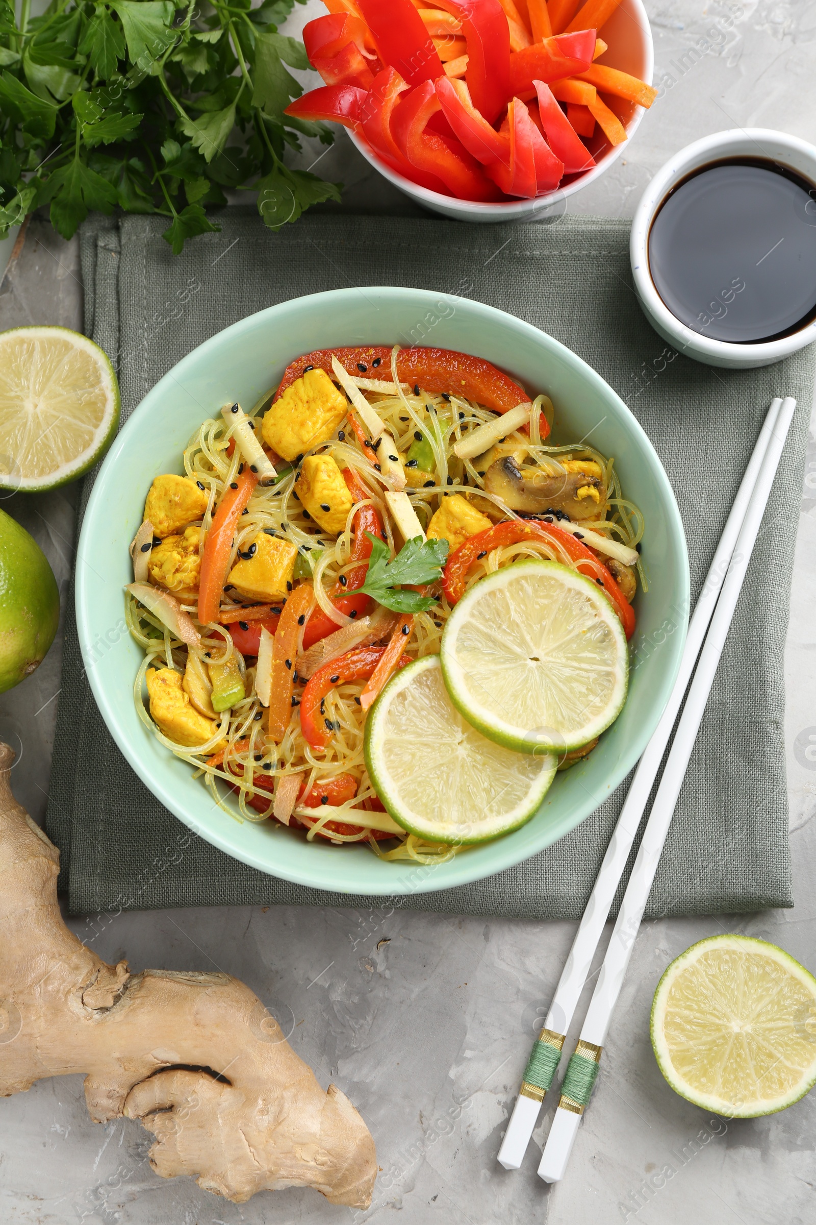 Photo of Stir-fry. Delicious cooked noodles with chicken and vegetables in bowl served on gray textured table, flat lay