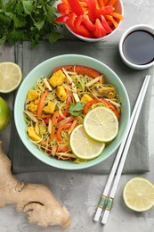 Photo of Stir-fry. Delicious cooked noodles with chicken and vegetables in bowl served on gray textured table, flat lay