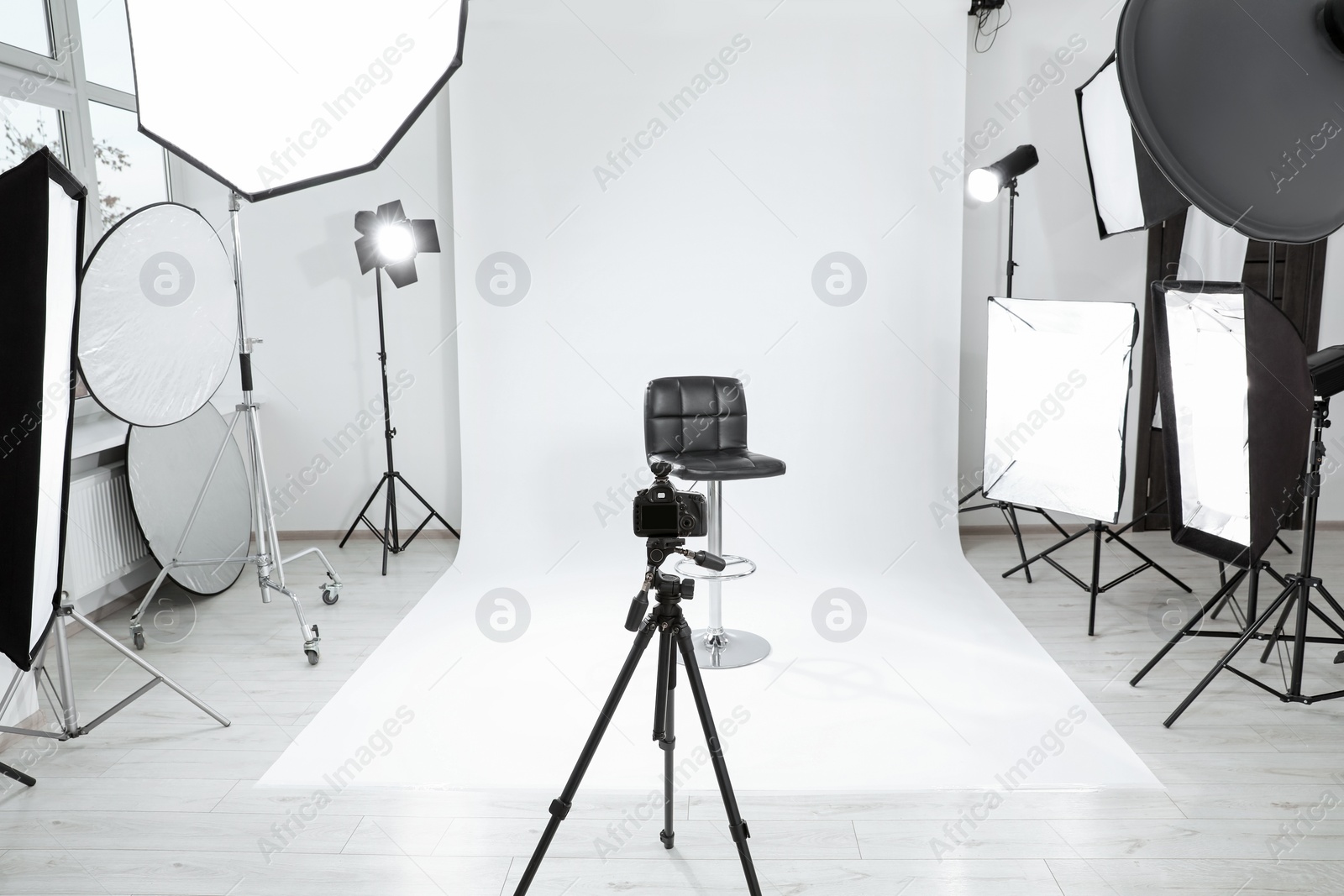 Photo of Tripod with camera, bar stool and professional lighting equipment in modern photo studio