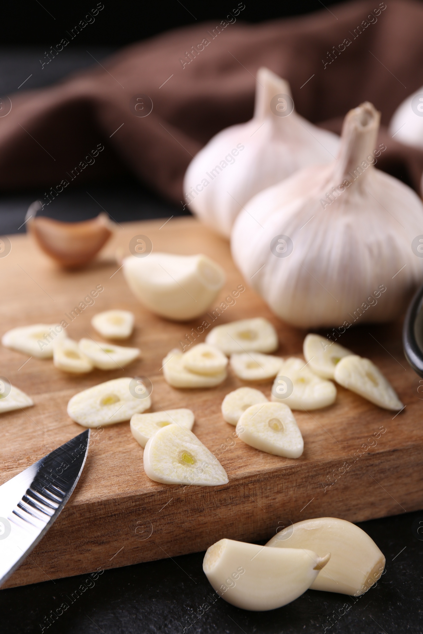 Photo of Aromatic cut garlic, cloves and bulbs on dark table, closeup