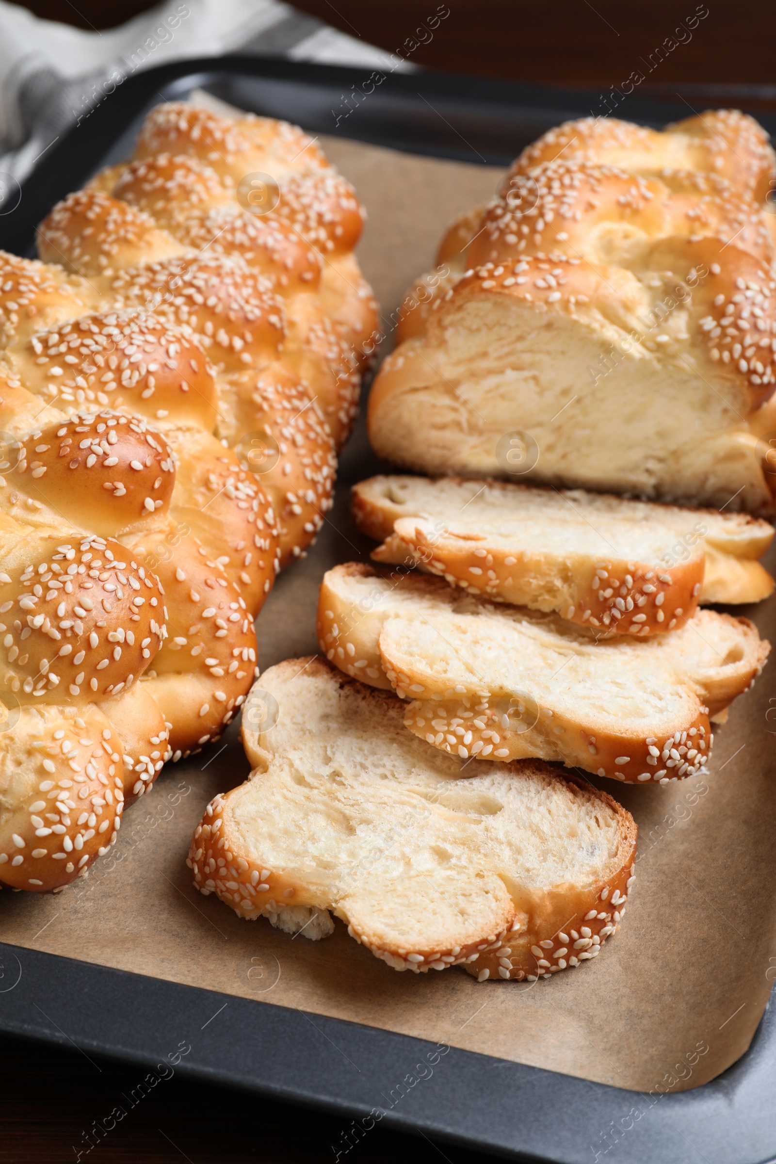 Photo of Baking tray with homemade braided bread on wooden table, closeup. Challah for Shabbat