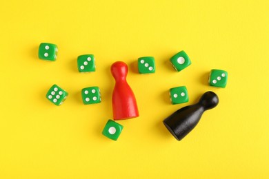 Photo of Many green dices and color game pieces on yellow background, flat lay