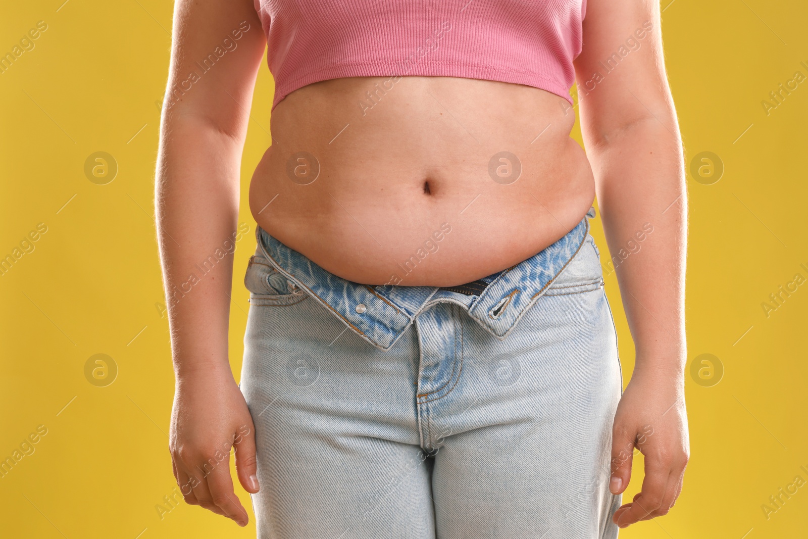 Photo of Woman with excessive belly fat on goldenrod background, closeup. Overweight problem