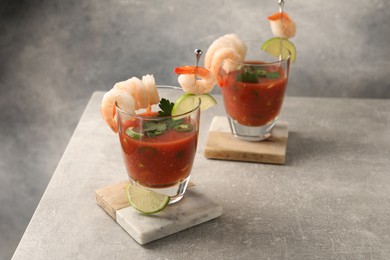 Tasty shrimp cocktail with sauce in glasses and lime on light grey table, space for text