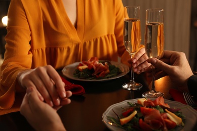 Couple with glasses of champagne at romantic dinner in restaurant, closeup