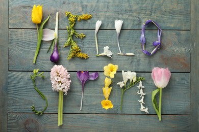 Photo of Words HELLO SPRING made of fresh flowers on light blue wooden table, flat lay