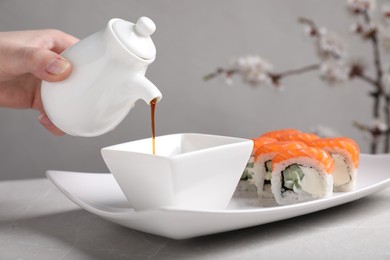 Photo of Woman pouring soy sauce for tasty sushi rolls at grey table, closeup