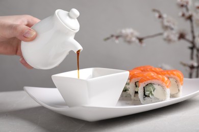 Woman pouring soy sauce for tasty sushi rolls at grey table, closeup