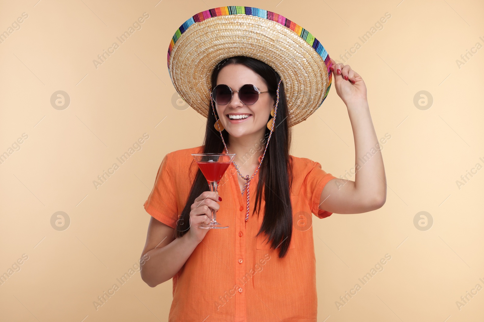 Photo of Young woman in Mexican sombrero hat with cocktail on beige background