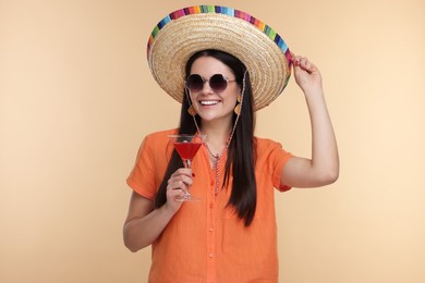 Photo of Young woman in Mexican sombrero hat with cocktail on beige background