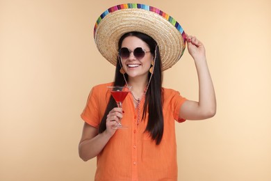 Young woman in Mexican sombrero hat with cocktail on beige background