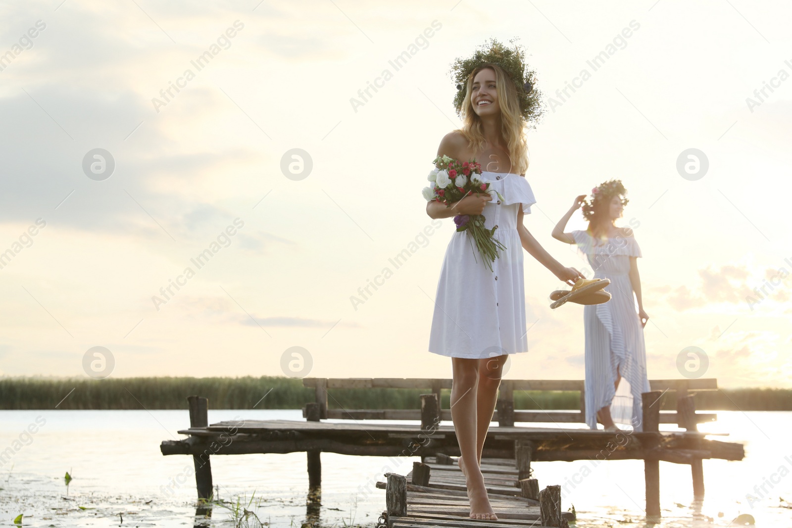 Photo of Young women wearing wreaths made of beautiful flowers on pier near river