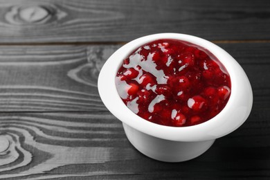 Photo of Fresh cranberry sauce in bowl on black wooden table, closeup. Space for text