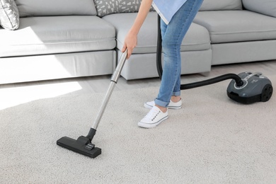 Woman removing dirt from carpet with vacuum cleaner at home