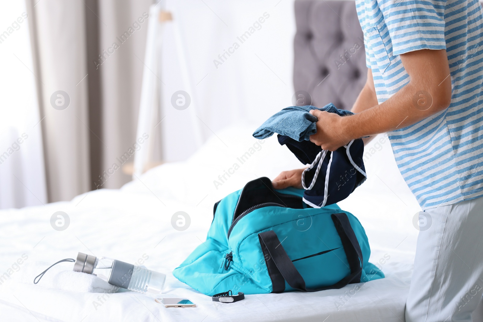 Photo of Young man packing sports stuff for training into bag in bedroom