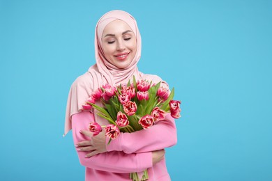 Photo of Happy woman in hijab with beautiful bouquet on light blue background. Space for text