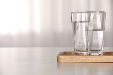 Photo of Glasses with water on white table against blurred background. Space for text