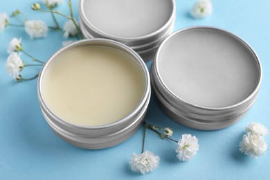 Photo of Different lip balms and gypsophila on light blue background, closeup