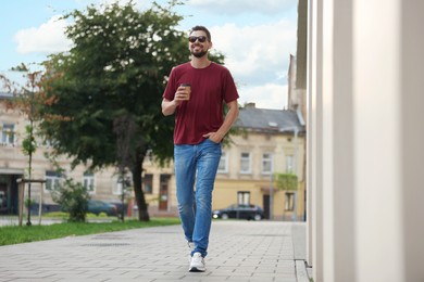 Photo of Handsome man with cup of drink walking on city street