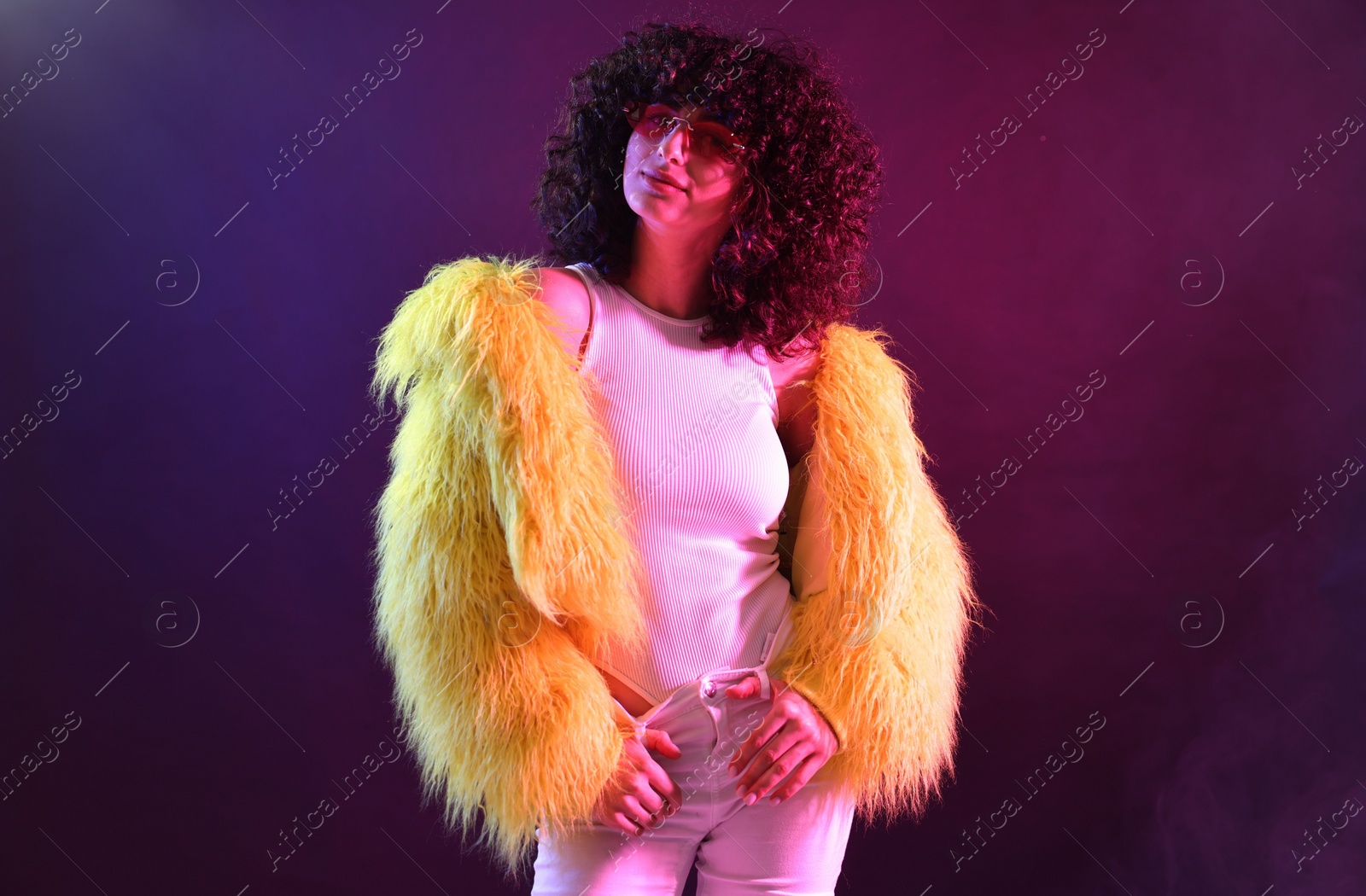 Photo of Beautiful young woman in yellow fur coat and sunglasses on color background in neon lights