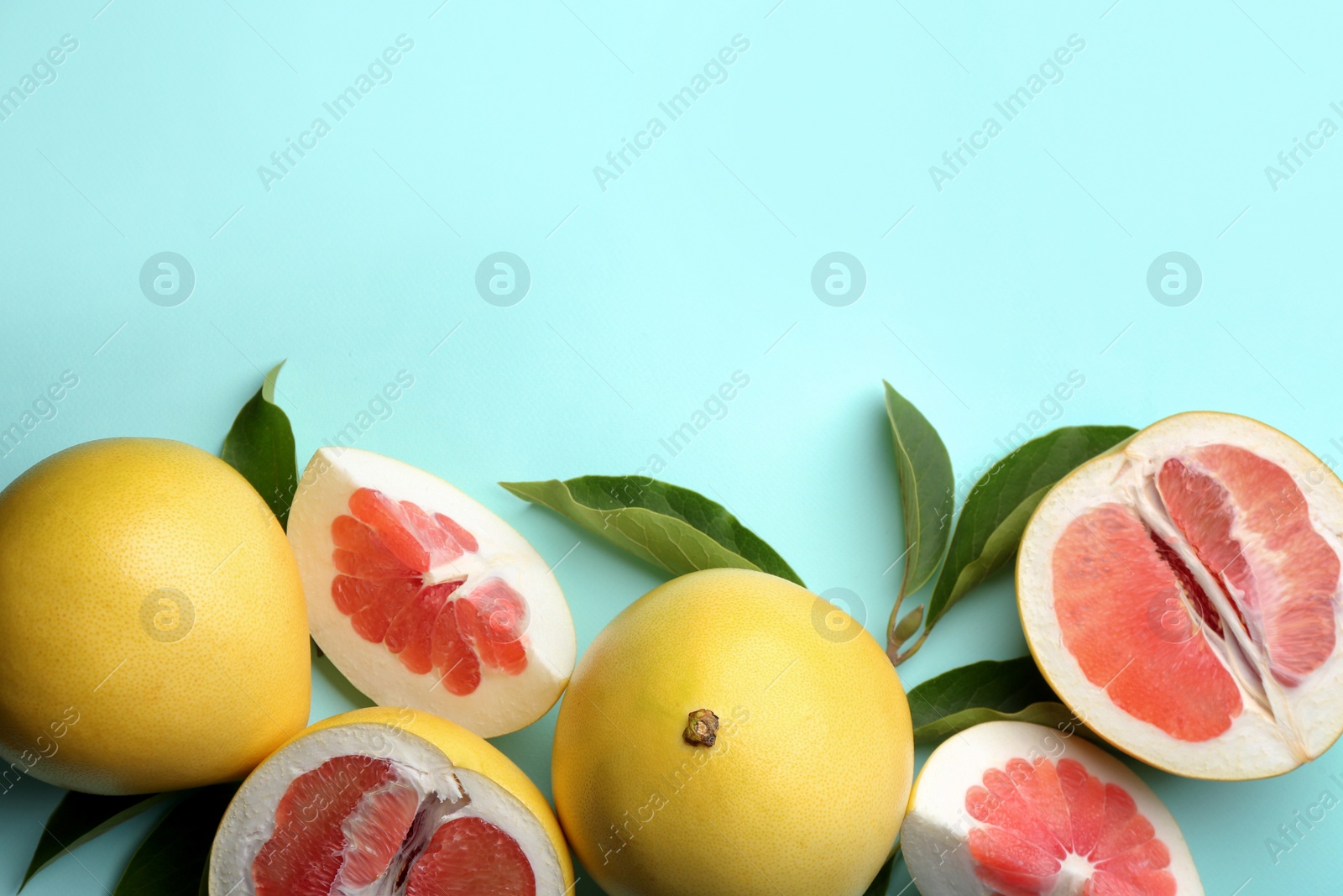 Photo of Fresh cut and whole pomelo fruits with leaves on turquoise background, flat lay. Space for text