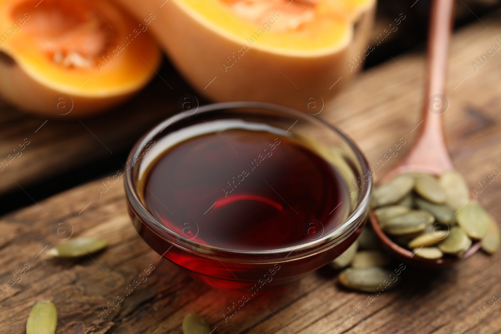 Photo of Glass bowl of pumpkin oil and seeds on wooden table, closeup