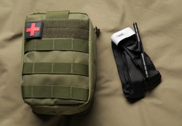 Photo of Military first aid kit and tourniquet on khaki fabric, flat lay