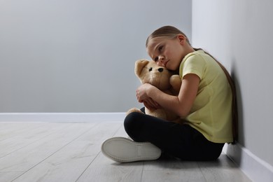 Child abuse. Upset girl with toy sitting on floor near grey wall, space for text