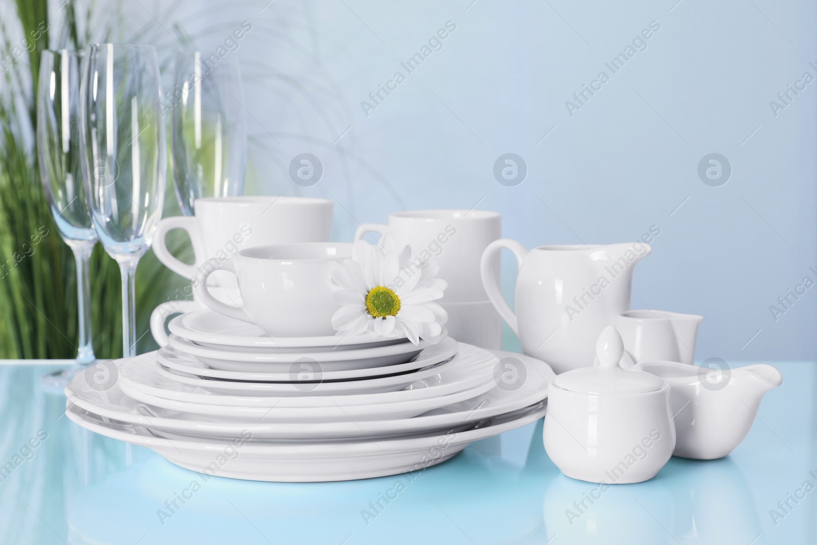 Photo of Set of clean dishware and flower on light blue table, closeup