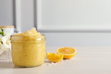 Body scrub in glass jar and lemon on light wooden table, space for text