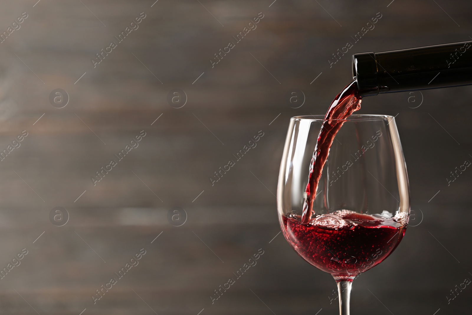 Photo of Pouring red wine into glass from bottle against blurred wooden background, closeup. Space for text